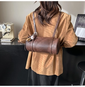 Detail of dark brown leather cylinder bag with embossed letters and baseball charm