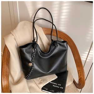 Detail of a minimalist black tote bag with braided charm on a wooden chair