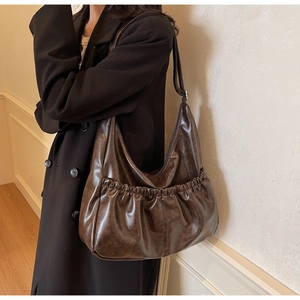Braune Hobo-Schultertasche aus Kunstleder mit Falten an Model in minimalistischem Raum