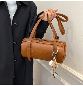 Detail of a brown leather cylinder bag featuring embossed texture and a baseball charm