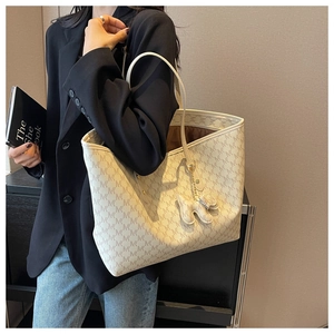 Macro detail of large cream tote bag with monogram texture and cute dog charm attachment