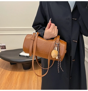 Brown leather cylinder bag with KCHADOUDO embossed lettering and yellow glove pendant detail