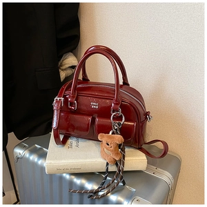 Détail d'un sac bowling en cuir verni rouge foncé avec charme d'ours sur une valise argentée