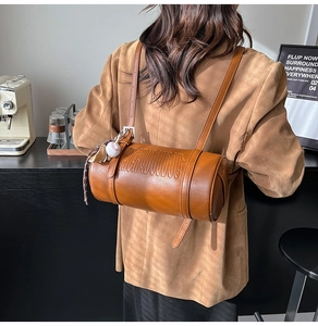 Detailed close-up of a caramel brown leather cylinder bag with athletic charms in a cafe