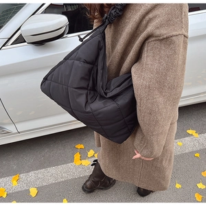 Detail of black quilted puffer tote bag with drawstrings shown in autumn street scene