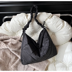 Detail of black quilted tote bag with ruffled shoulder strap and bow on white cushion