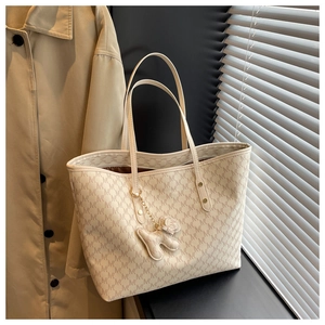 Detailed view of beige tote bag with monogram patterns and a cute bear bag charm accessory