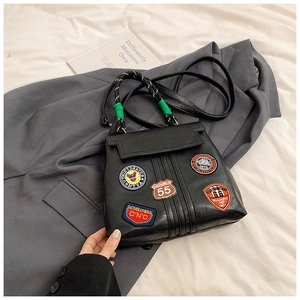 Detail of black faux leather bag with vintage embroidery patches and woven handle