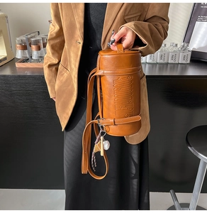 Close-up of caramel brown cylindrical leather bag with embossed text and creative baseball charm
