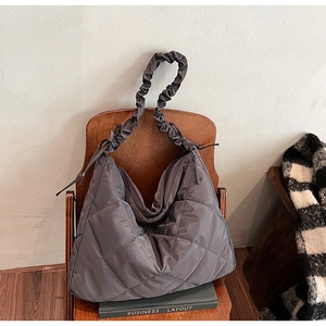 Detail of grey quilted tote bag with scrunchie strap draped over a wooden chair