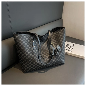 Detail of black monogram tote bag with animal charm on a luxury grey leather sofa