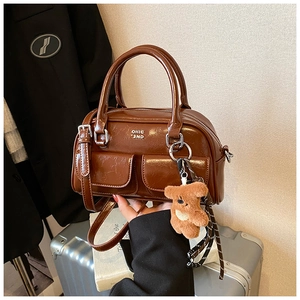 Détail du sac bowling marron vintage avec poches frontales, breloque ours et foulard