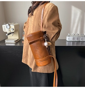 Detail view of vintage brown leather cylinder bag with embossed logo and baseball charm