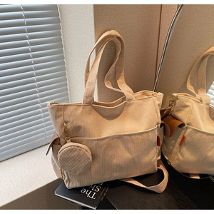 Detail of beige corduroy tote bag featuring front pockets and round zipper charm
