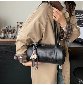 Detail view of black cylinder bag with baseball charm and embossed leather texture