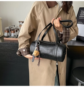 Close-up of black cylinder shoulder bag with embossed letters and cute animal charm