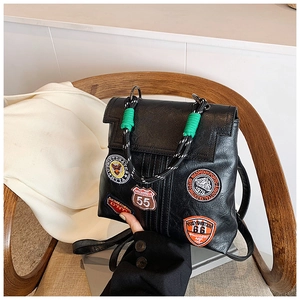 Detail view of vintage black PU backpack with colorful embroidery patches on a wooden chair