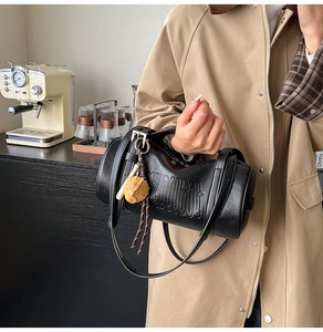 Detail of black cylindrical leather bag with embossed letters and a cute animal charm