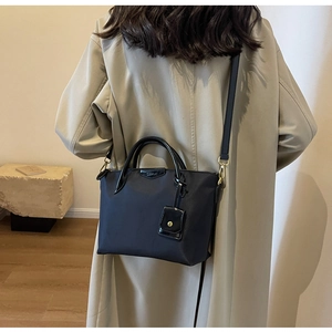 Detail of a black textured crossbody bag with cylindrical handles and a mini pouch