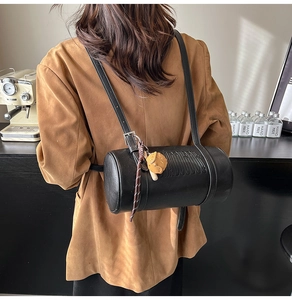 Close-up of black cylinder leather bag on a model featuring embossed letters and plush charm