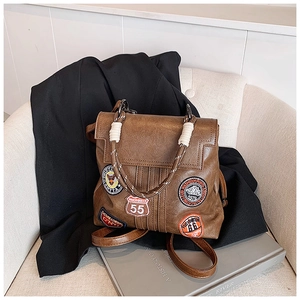 Detail of vintage brown leather backpack featuring embroidered patches and woven handle