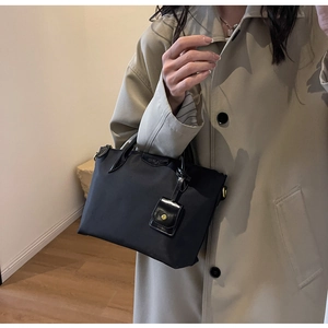 Detail of black nylon tote bag with leather logo tag and mini purse charm on model