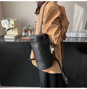 Detail of black cylindrical leather shoulder bag with embossed texture in a cafe setting