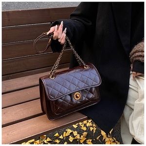 Close-up of quilted coffee brown shoulder bag featuring gold chain and turn-lock detail