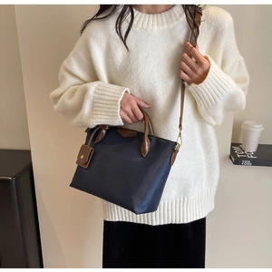 Detail of navy nylon dumpling bag with brown leather handles and a side pouch accessory