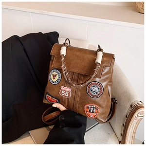 Detail of vintage brown leather backpack featuring embroidered patches and woven rope handle