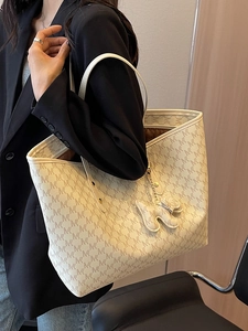 Minimalist beige tote bag with letter prints and a dog charm worn by a model in a black suit