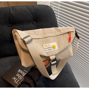 Dettaglio della borsa a tracolla in nylon beige con patch smiley giallo e zip arancione