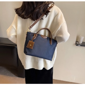 Close-up of a dark blue nylon crossbody bag with brown leather straps shown on a model