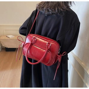 Detail of red bowling bag with side bow design and crossbody strap on black outfit