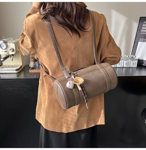Detail of a brown leather cylinder bag with baseball charms on a lifestyle model