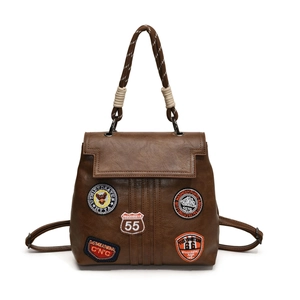 Detail of vintage brown leather backpack featuring woven handle and retro embroidery patches