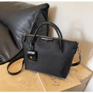 Detail shot of a black nylon tote with leather handles and gold zipper on a stone base