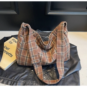 Close-up of brown plaid tote bag with adjustable strap on a leather jacket background