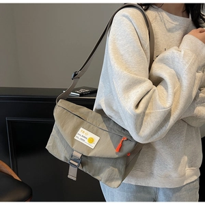 Dettaglio della borsa a tracolla in nylon verde oliva con stemma smiley giallo e zip arancione