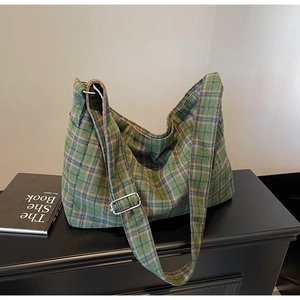 Close-up of green plaid tote bag with wide adjustable shoulder strap and metal buckle