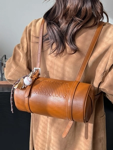 Brown vintage cylinder pillow bag in soft leather with embossed letters and ball charm