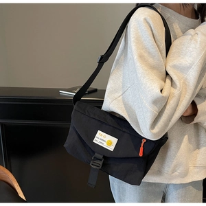 Dettaglio della borsa a tracolla in nylon nero con tracolla regolabile e zip arancione