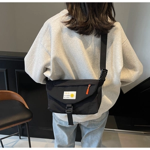 Dettaglio della borsa messenger in nylon nero con toppa sorridente e cinturino arancione