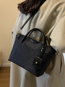 Minimalist black tote bag with glossy handles worn by a woman in a stylish beige coat
