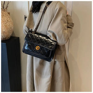 Detailed side view of black quilted leather handbag with gold chain strap on model