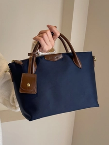 Minimalist navy blue nylon tote bag with brown leather handles and brand logo