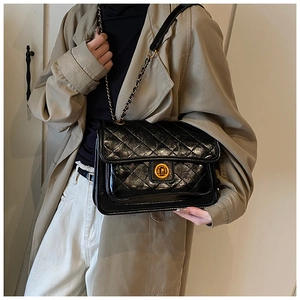 Detail view of black quilted leather shoulder bag with gold chain strap on a model