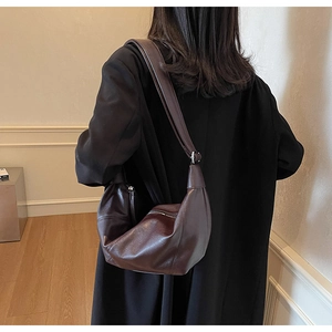 Borsa a mezzaluna in pelle marrone scuro indossata da una modella per un look minimalista