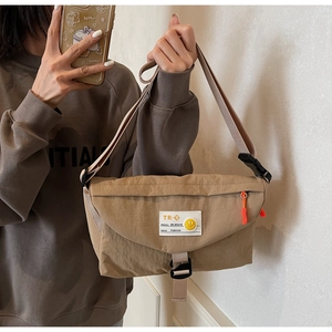 Dettaglio della borsa a tracolla in nylon kaki con patch smiley e tirazip arancione