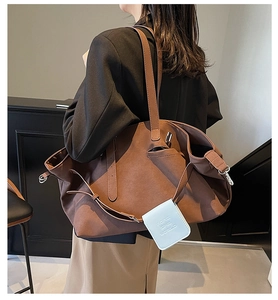 Dettaglio borsa tote in pelle scamosciata marrone con tracolla e ciondolo azzurro
